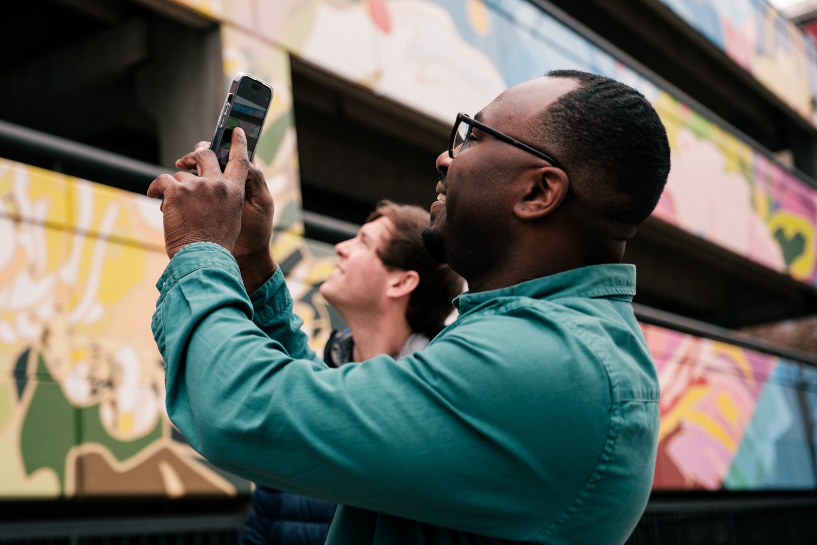 Photo of man holding up a mobile phone to take a photo of a mural on a building